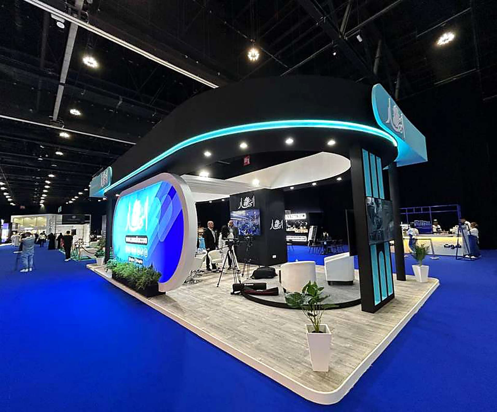 Curved black-and-teal media pavilion with a backlit LED portal and broadcast cameras set up for live interviews