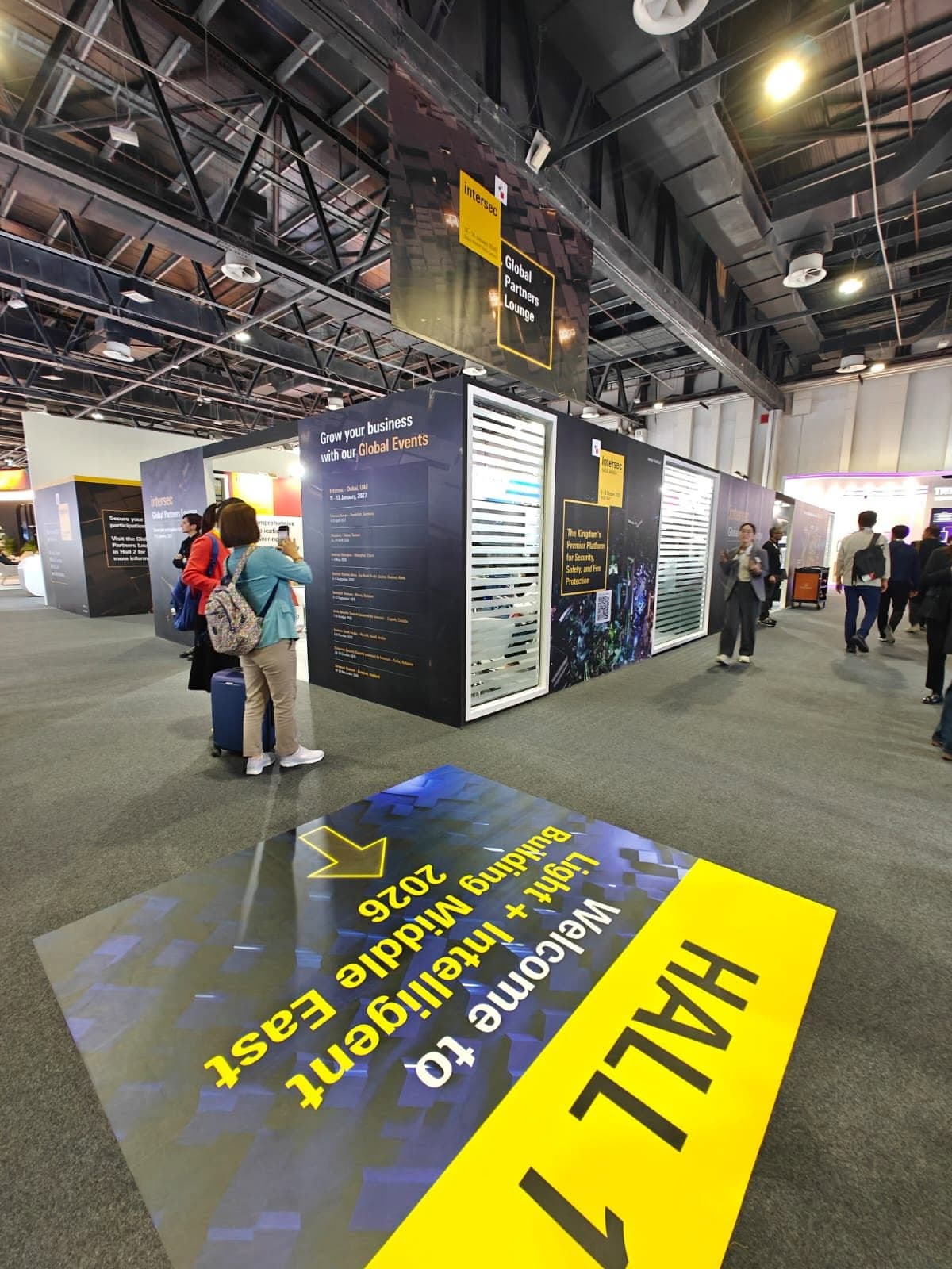 Suspended wayfinding banner and printed hall-entrance floor graphic at a Dubai trade show
